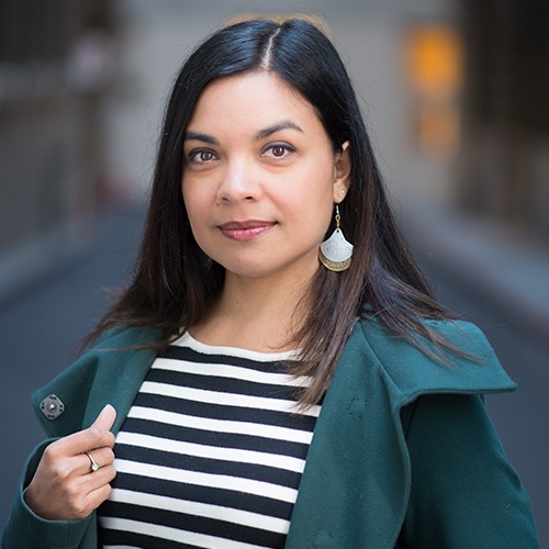 Headshot of Maya Borgueta, San Francisco Psychologist, standing on the street in downtown San Francisco. She is a Millennial Filipinx woman with long hair and is wearing a green goat and striped shirt.