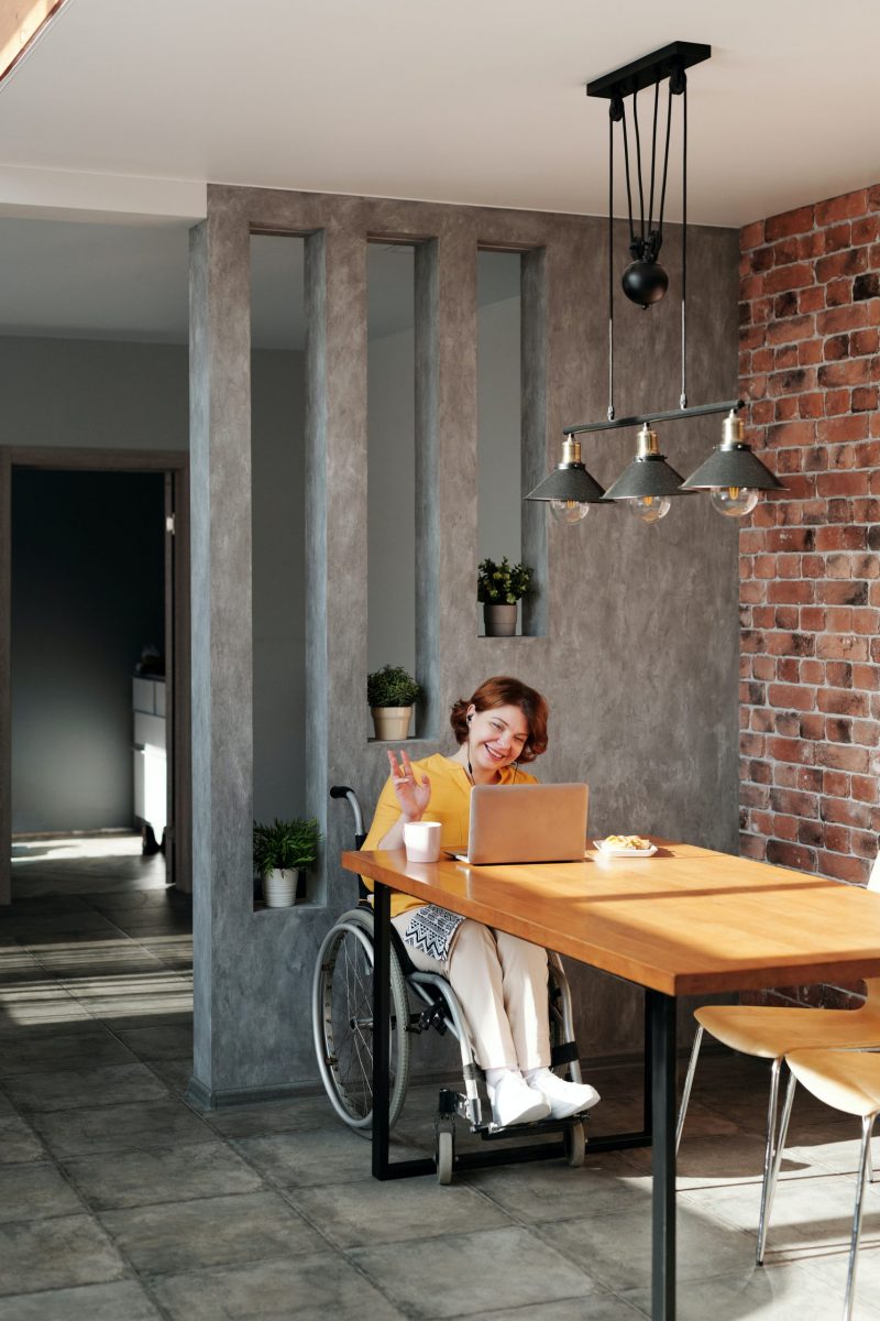 Woman using laptop to work from home. She is a wheelchair user and is in a home with modern industrial decor.