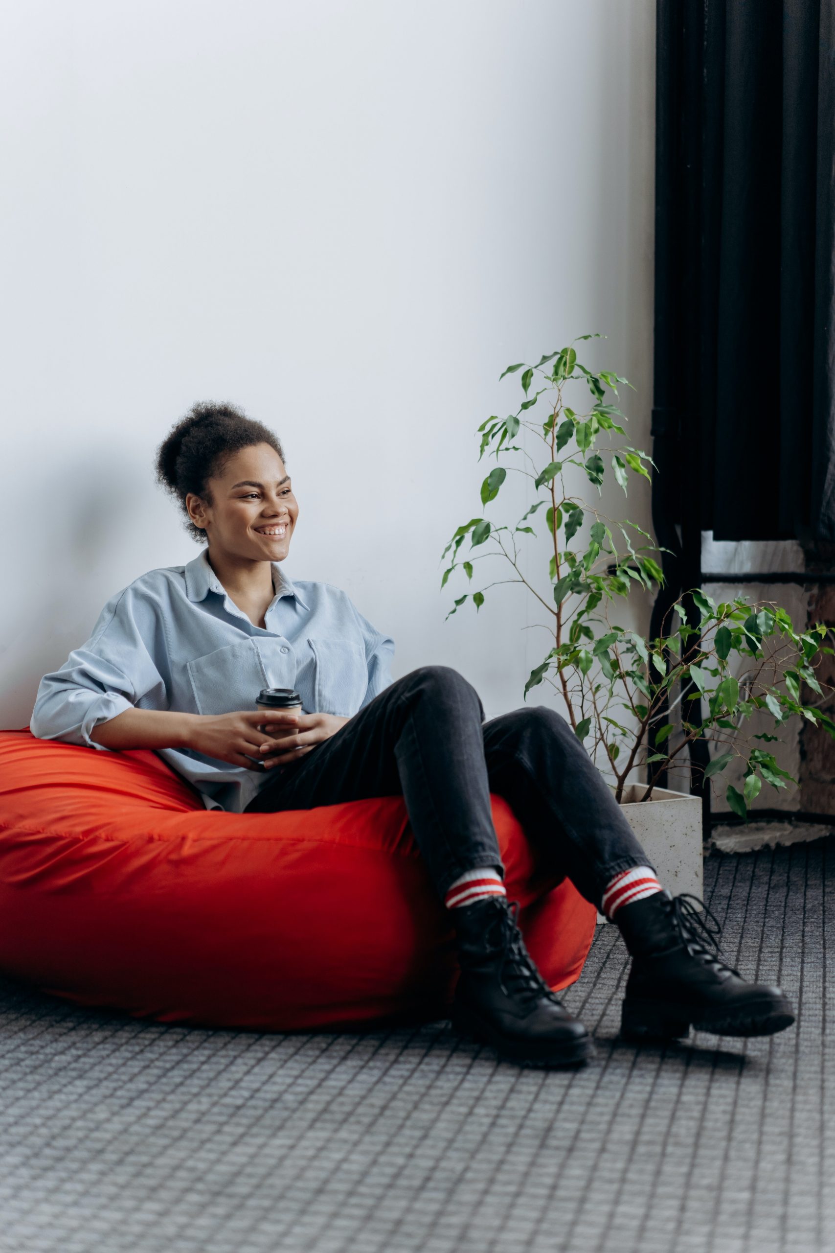 Young Black tech worker sits in a bean bag chair with a cup of coffee in hand.