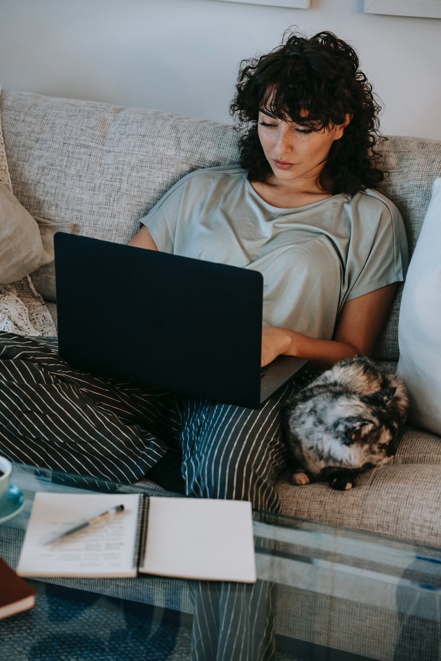 Woman in casual attire attending an online therapy session from her couch. A black and white cat sits next to her.