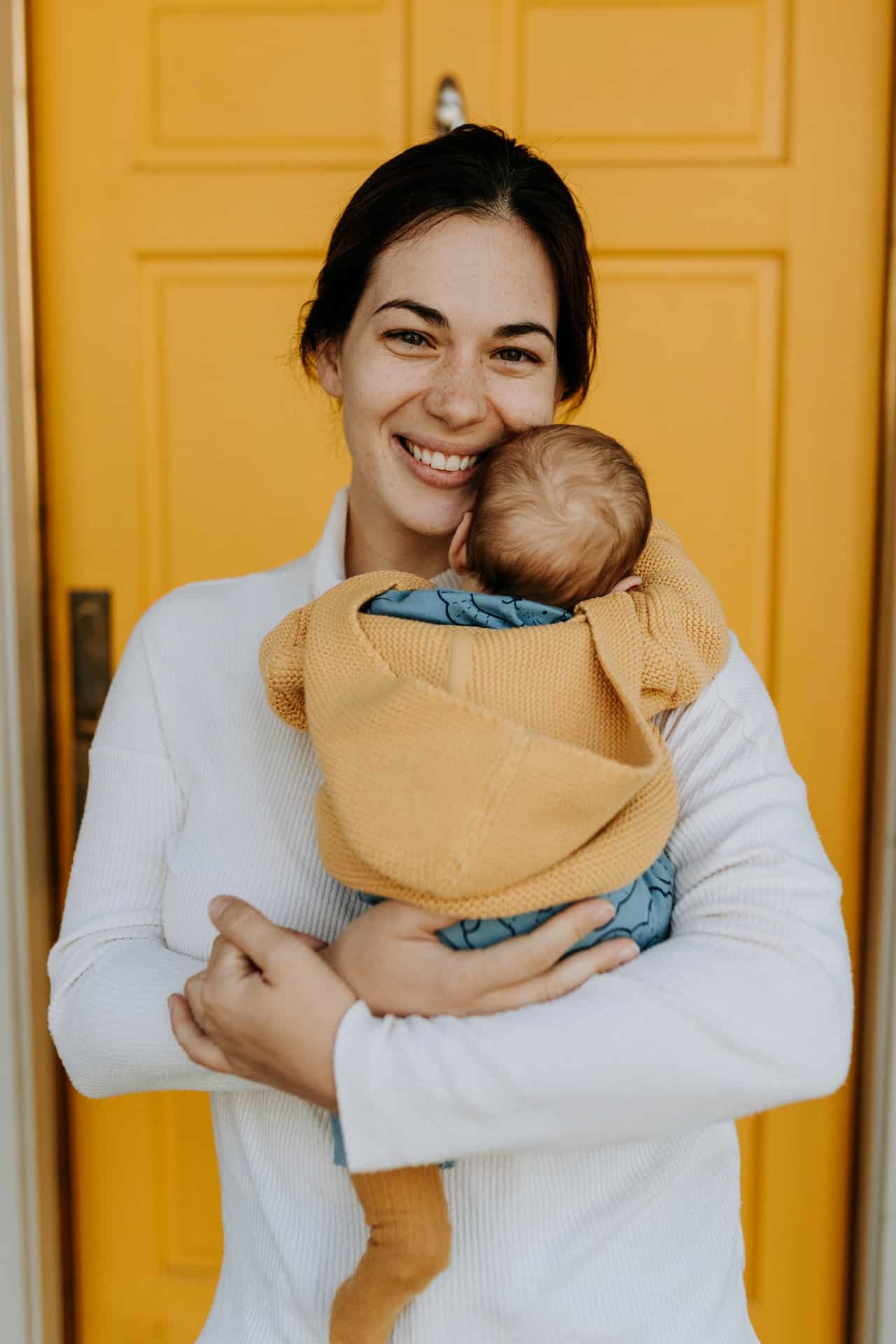 Woman holding newborn in front of a bright yellow door.