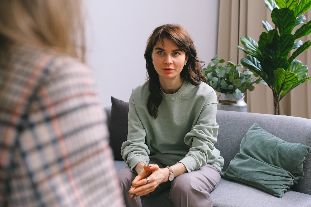 Woman sitting on a couch talking to a therapist, who is partially visible over her shoulder.