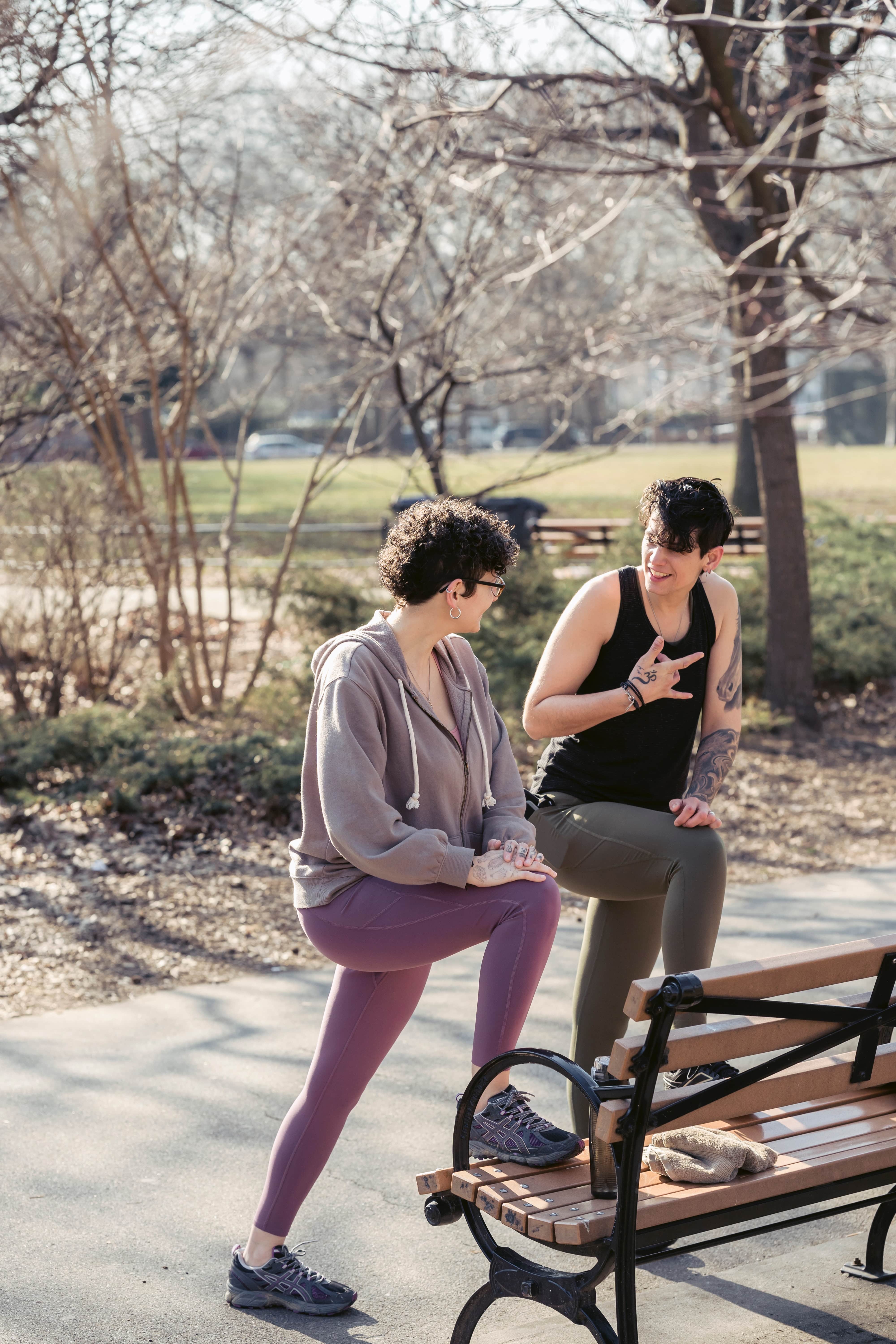 Two friends stretching together at a park bench as they prepare to go for a run