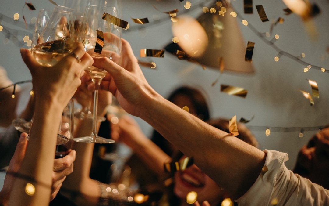 Hands holding champagne glasses in a toast, with gold confetti raining down around them.