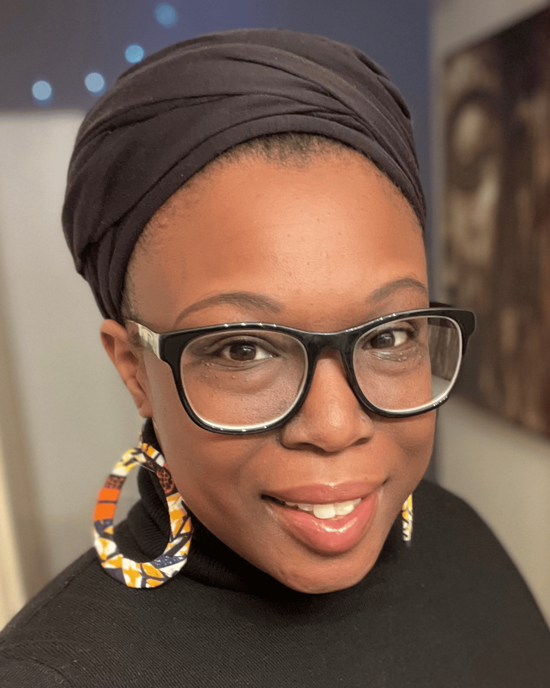 Headshot photo of Shahneka Dupart, ACSW a therapist in San Francisco, California. Shahneka is a Black woman wearing glasses, large colorful earrings, and a black head wrap.