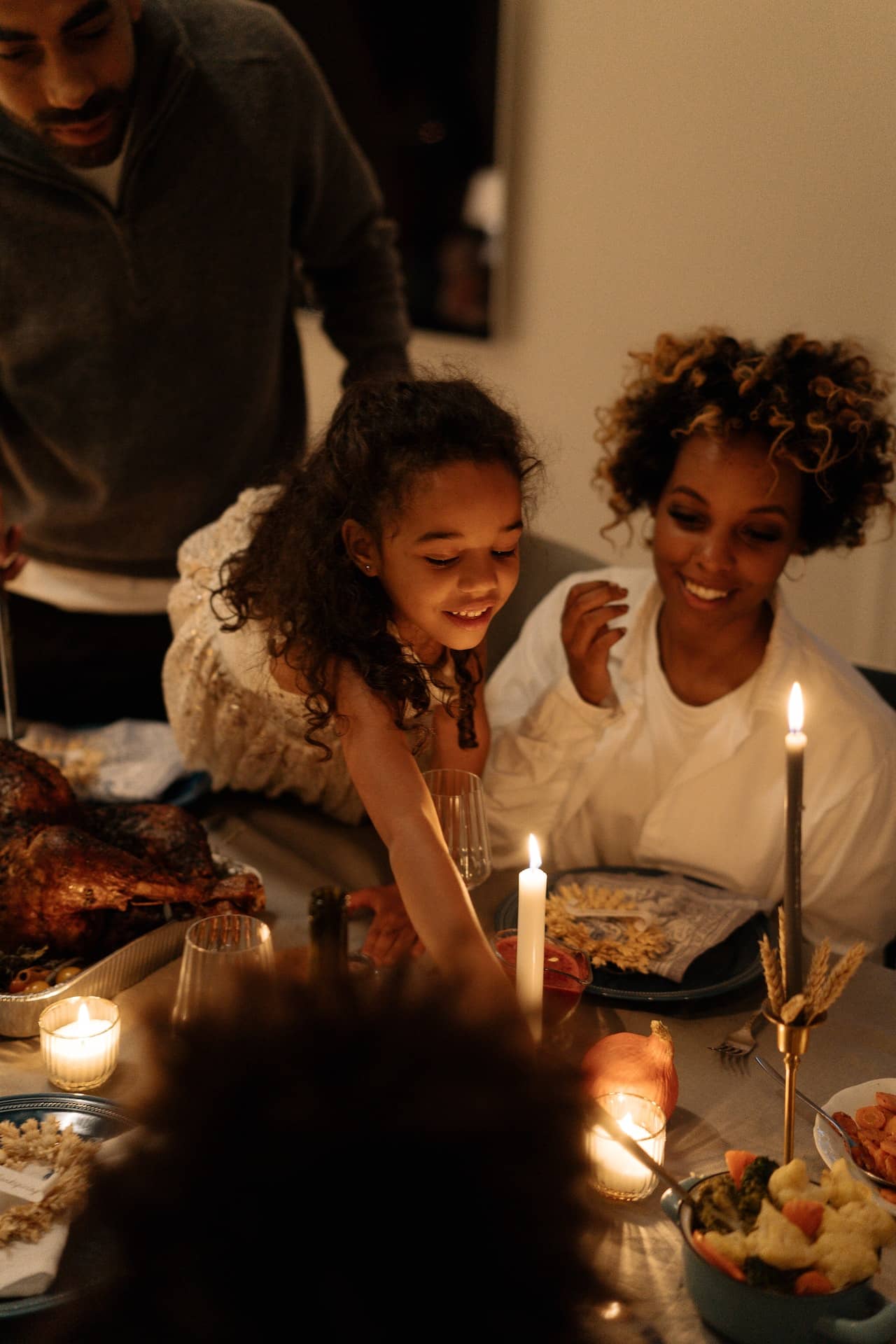 A mother and young daughter at a holiday dinner together, lit by candlelight.
