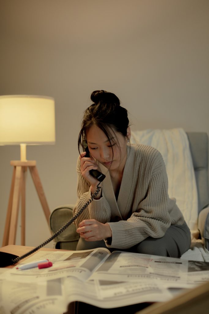 Professionally dressed Asian American woman on the phone while she browses the classified ads in a newspaper. 