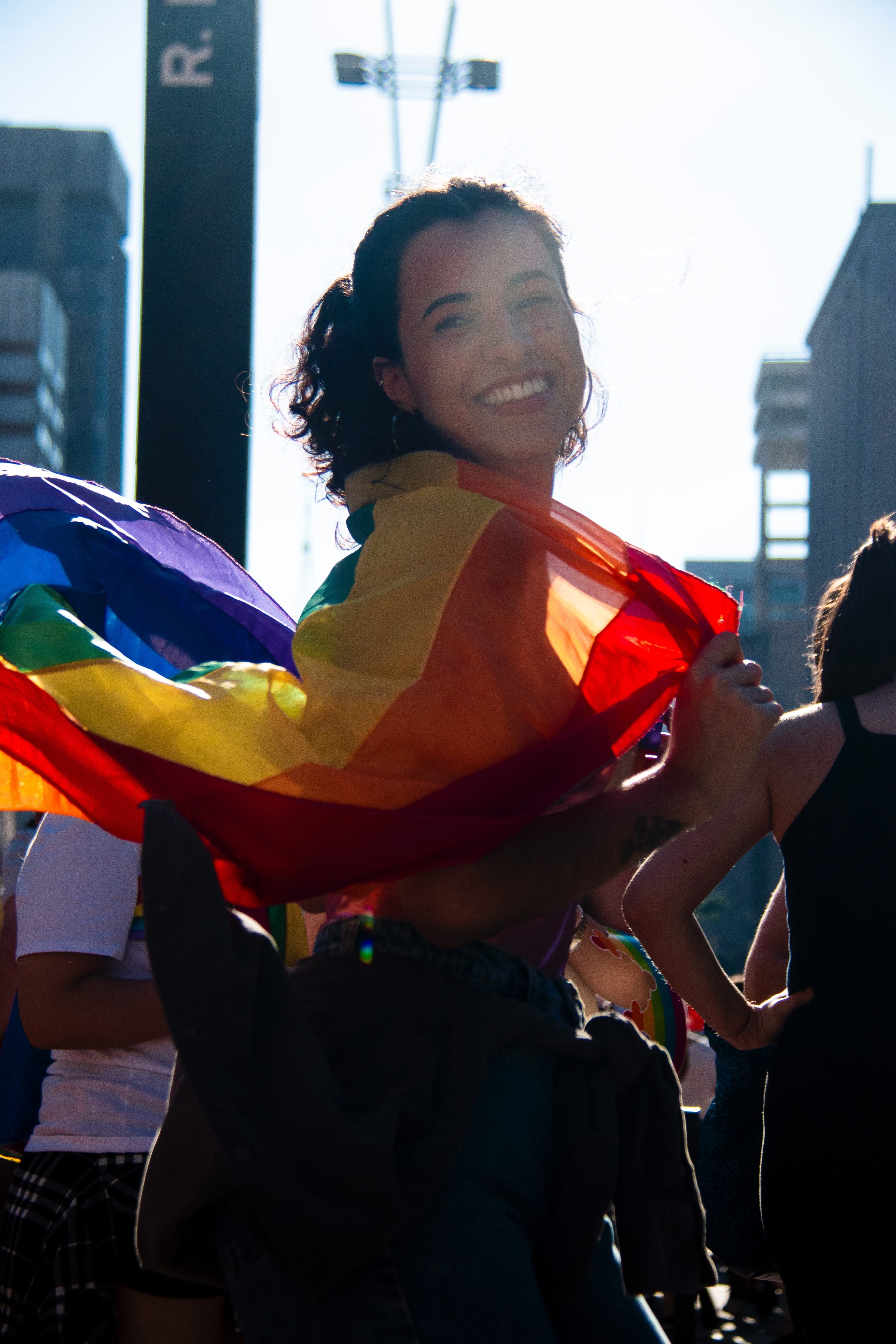 A femme person with dark hair poses with a rainbow pride flag during a San Francisco LGBTQ+ pride event.