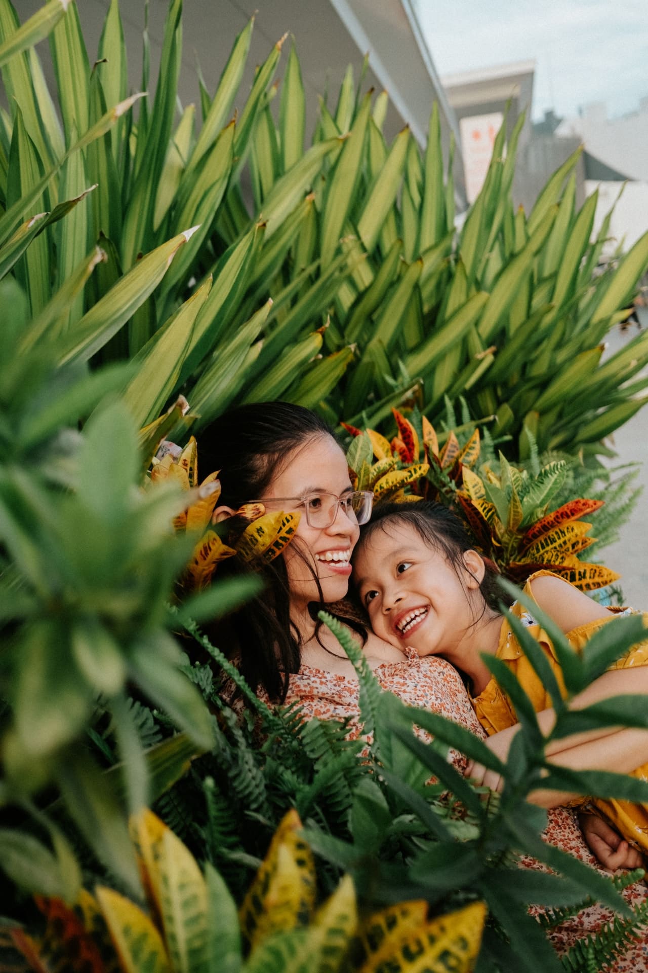 Mother and daughter looking playful and happy against a background of tropical plants.
