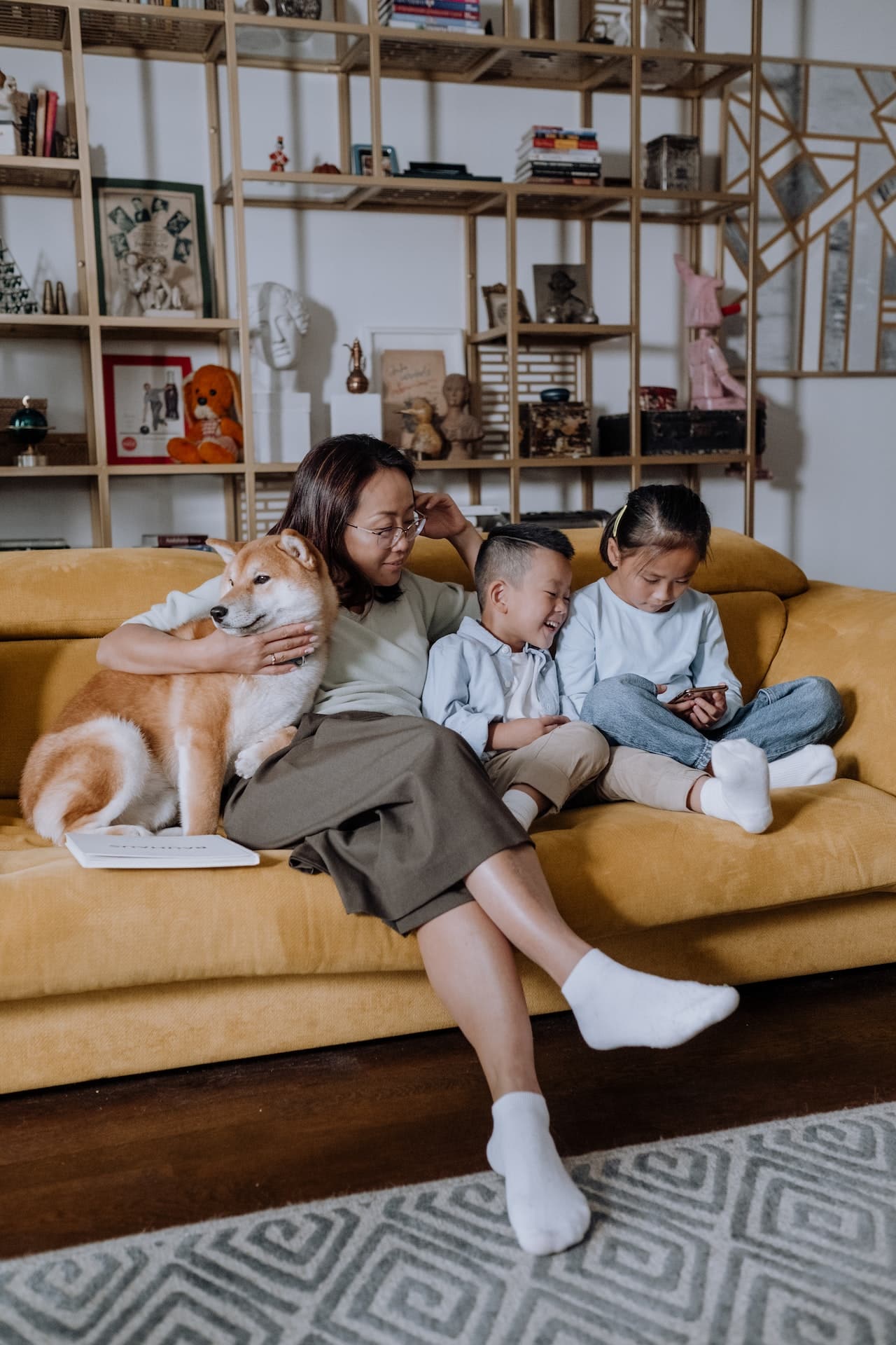 An Asian woman sitting on her sofa in a living room with two children.