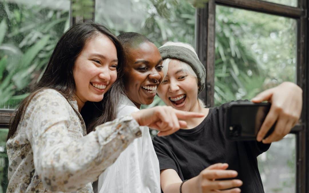 A multiracial group of three smiling women take a selfie together.