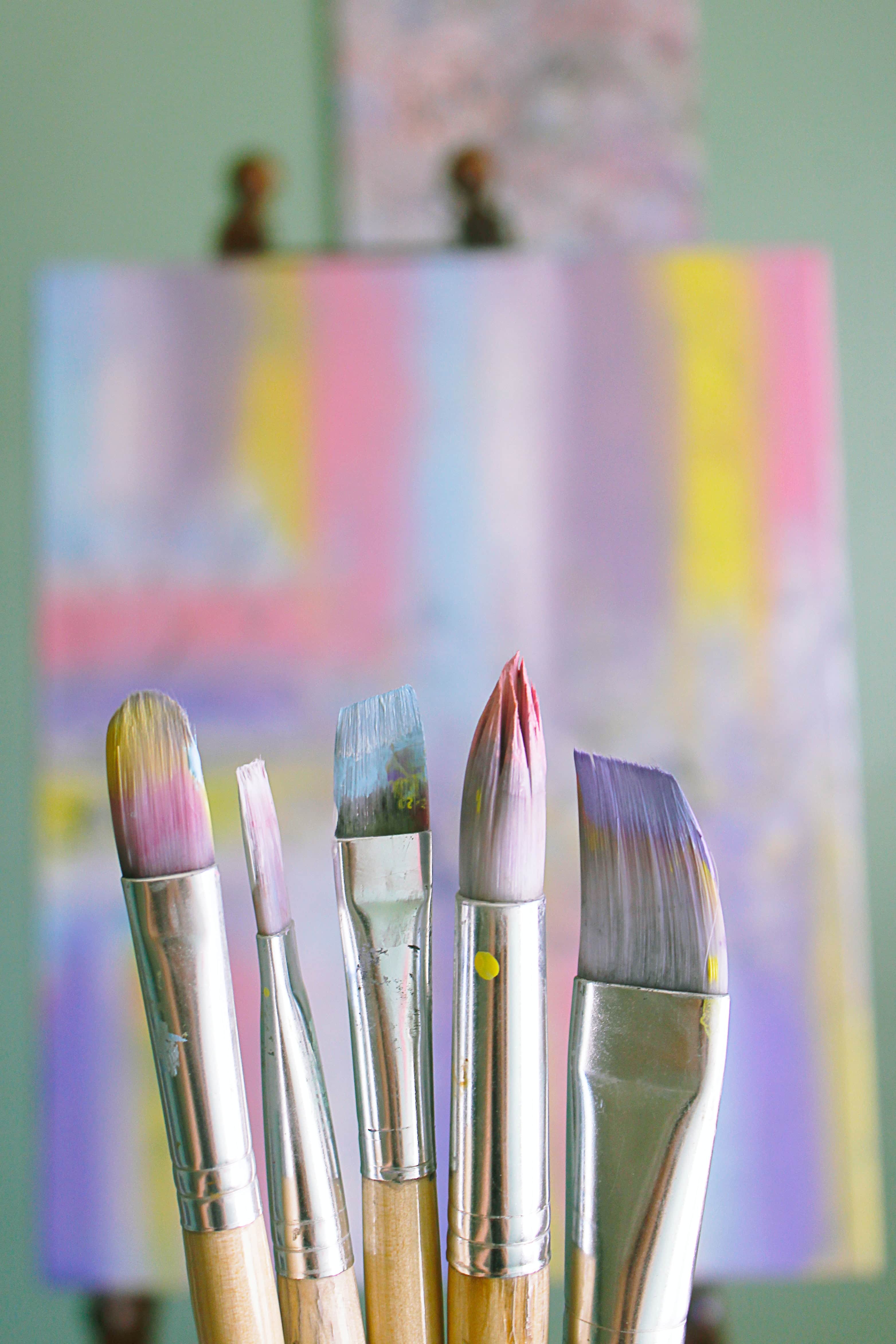 Image of paintbrushes covered in colorful paints in front of an out of focus canvas