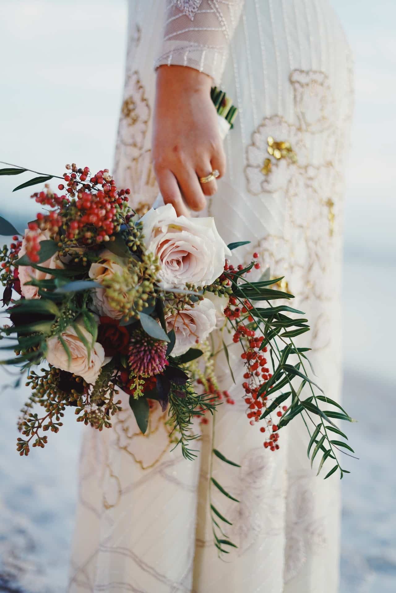 Close up photo of a person in a bridal gown holding a bouquet of flowers, visible only from hip down.