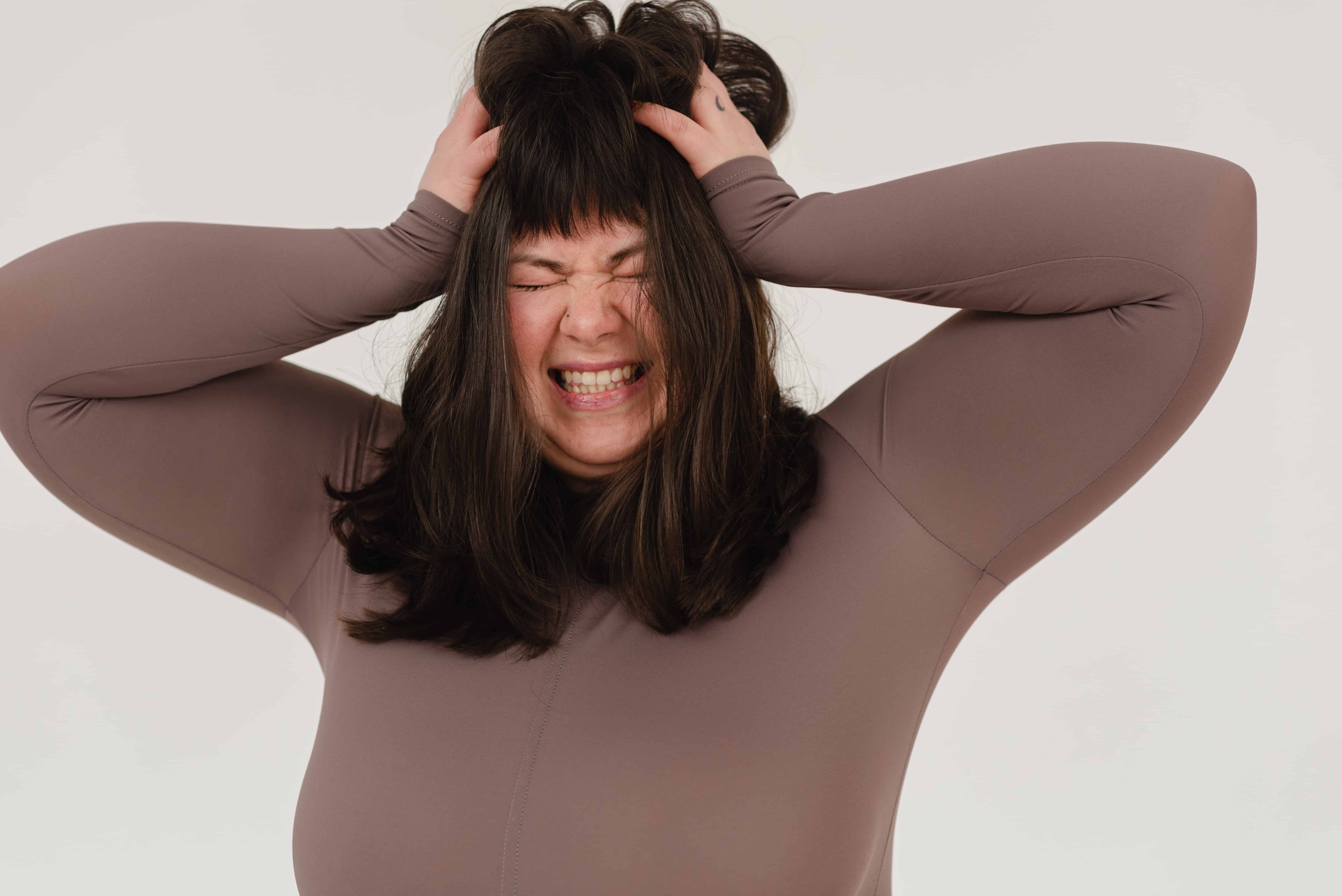 Stressed out woman grabs at her hair in frustration, stock photo.