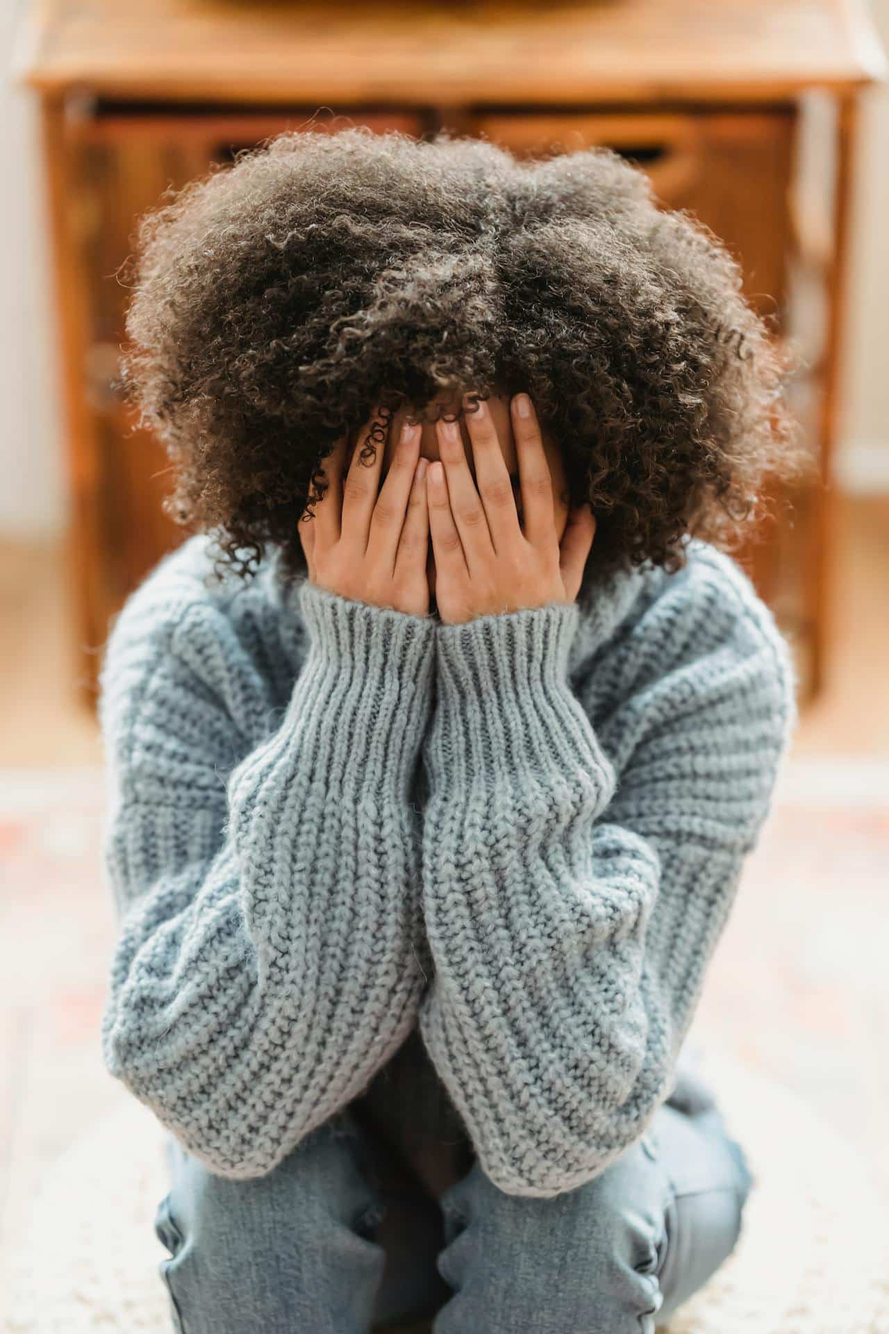 A Black woman with natural hair covers her face, as though stressed out or embarrassed.