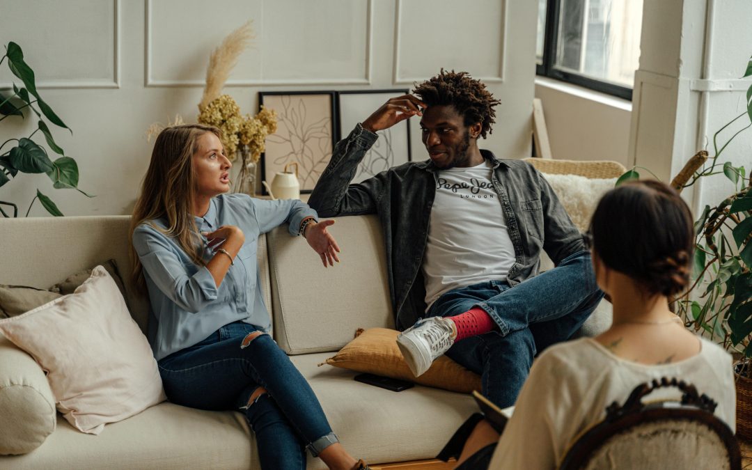 a white woman and a Black man sitting on a couch in a therapist's office, with the therapist mostly out of frame.