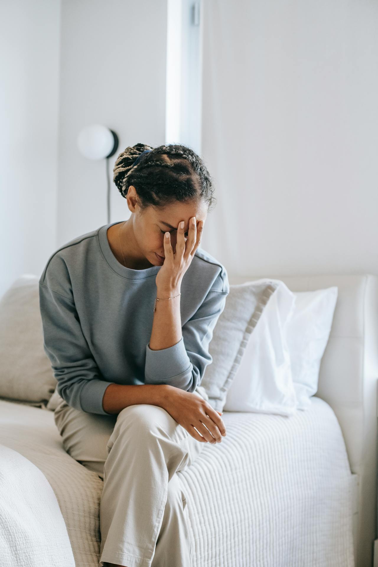 A black woman wearing casual clothes holds her head with her hands.