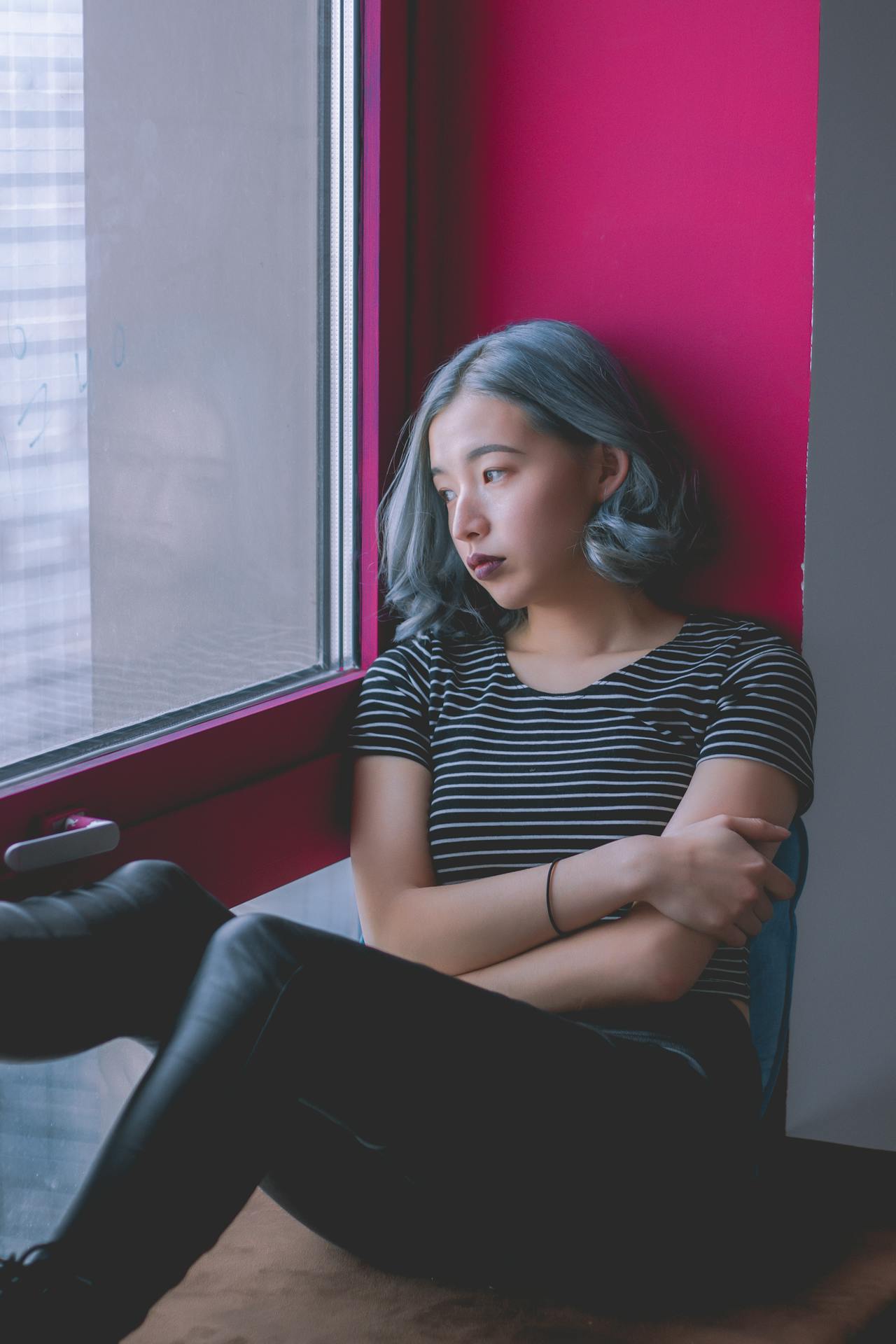 A young Asian woman with blue hair looks out the window.