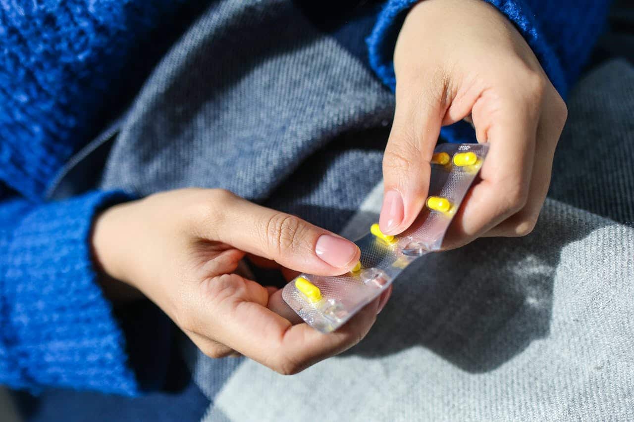 Close up of a woman's hands taking a pill out of a blister pack.