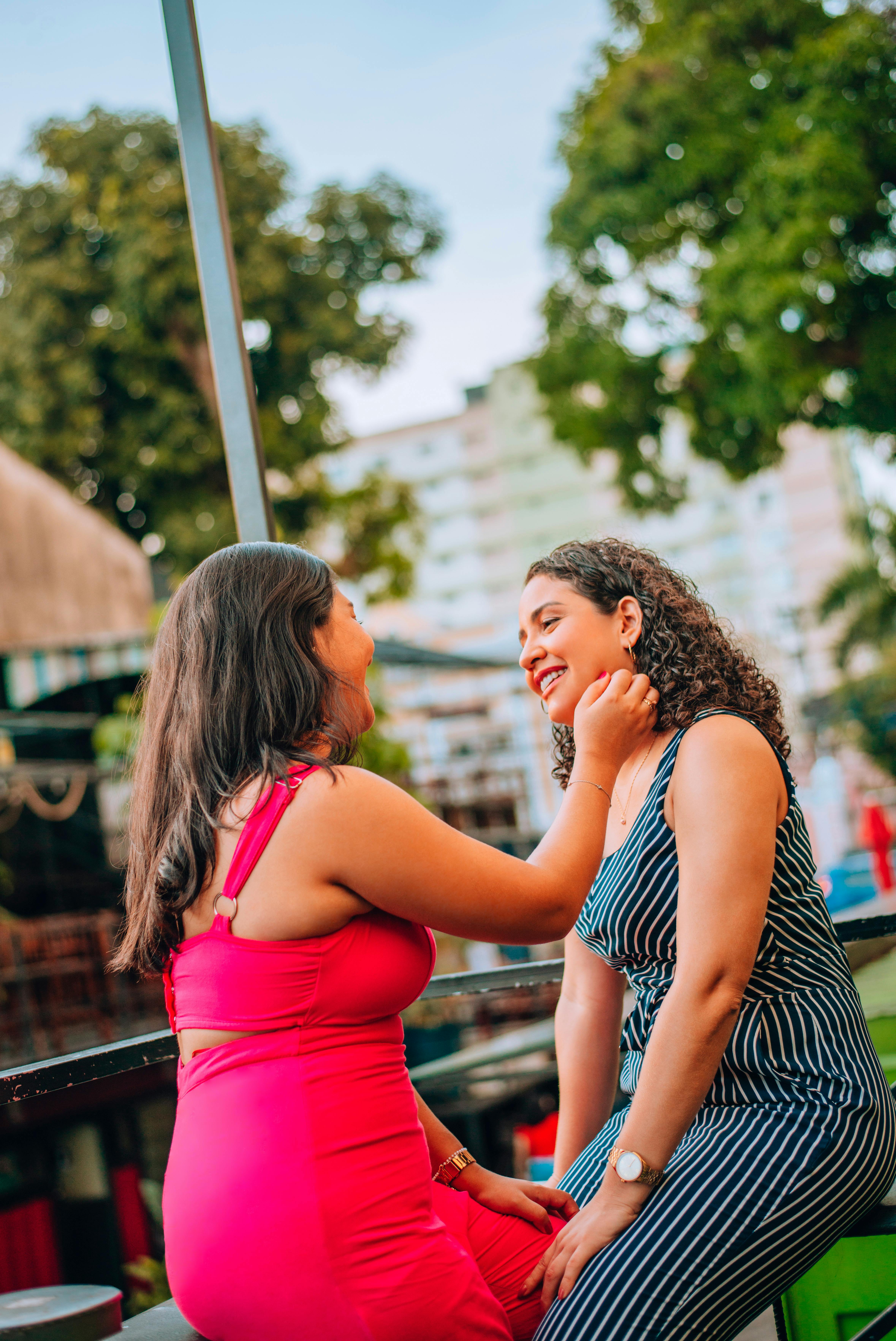 Two women sitting together outside on a date, looking at each other's faces and smiling.