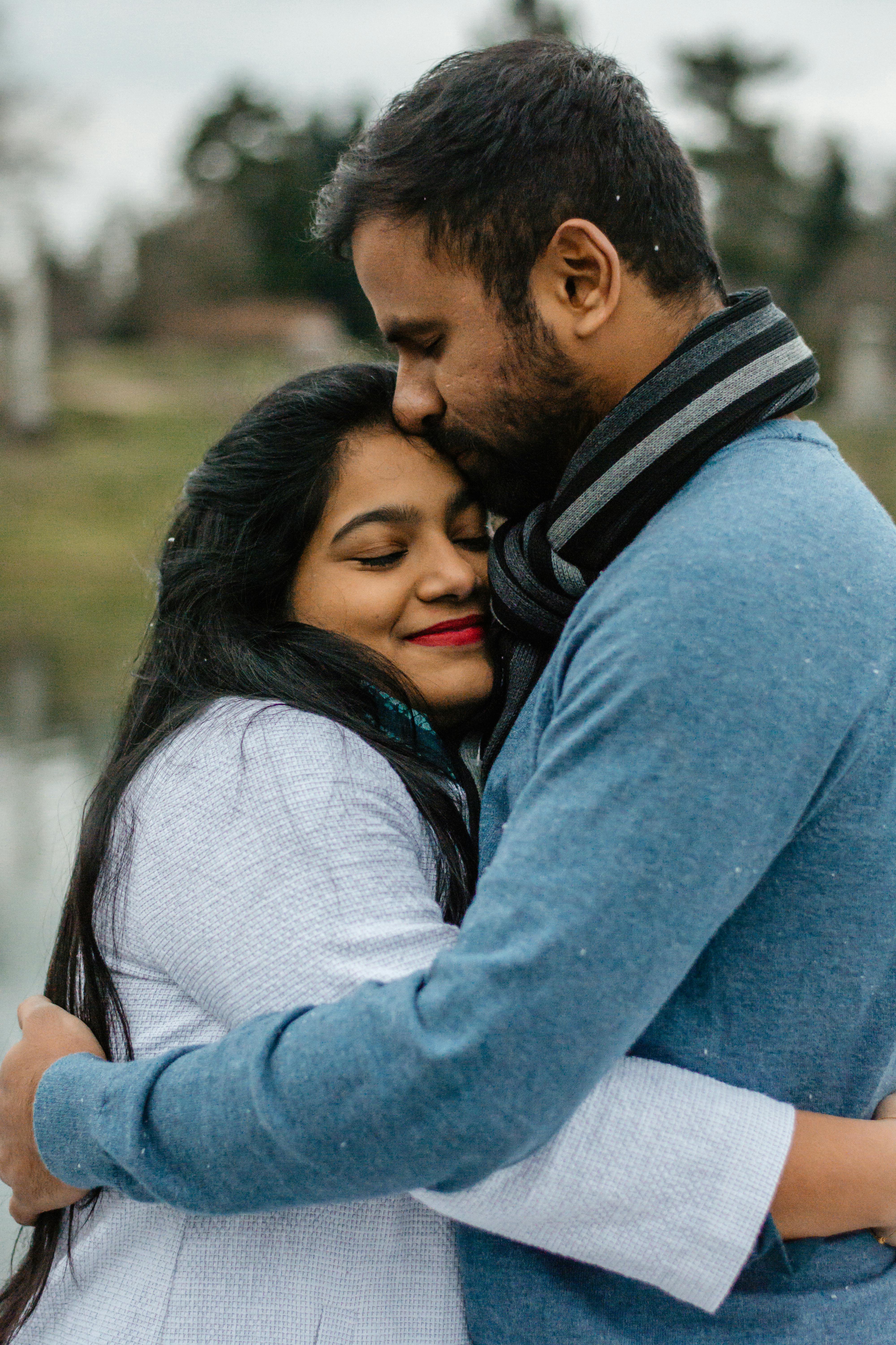 A man and a woman of South Asian heritage, embracing happily outside.