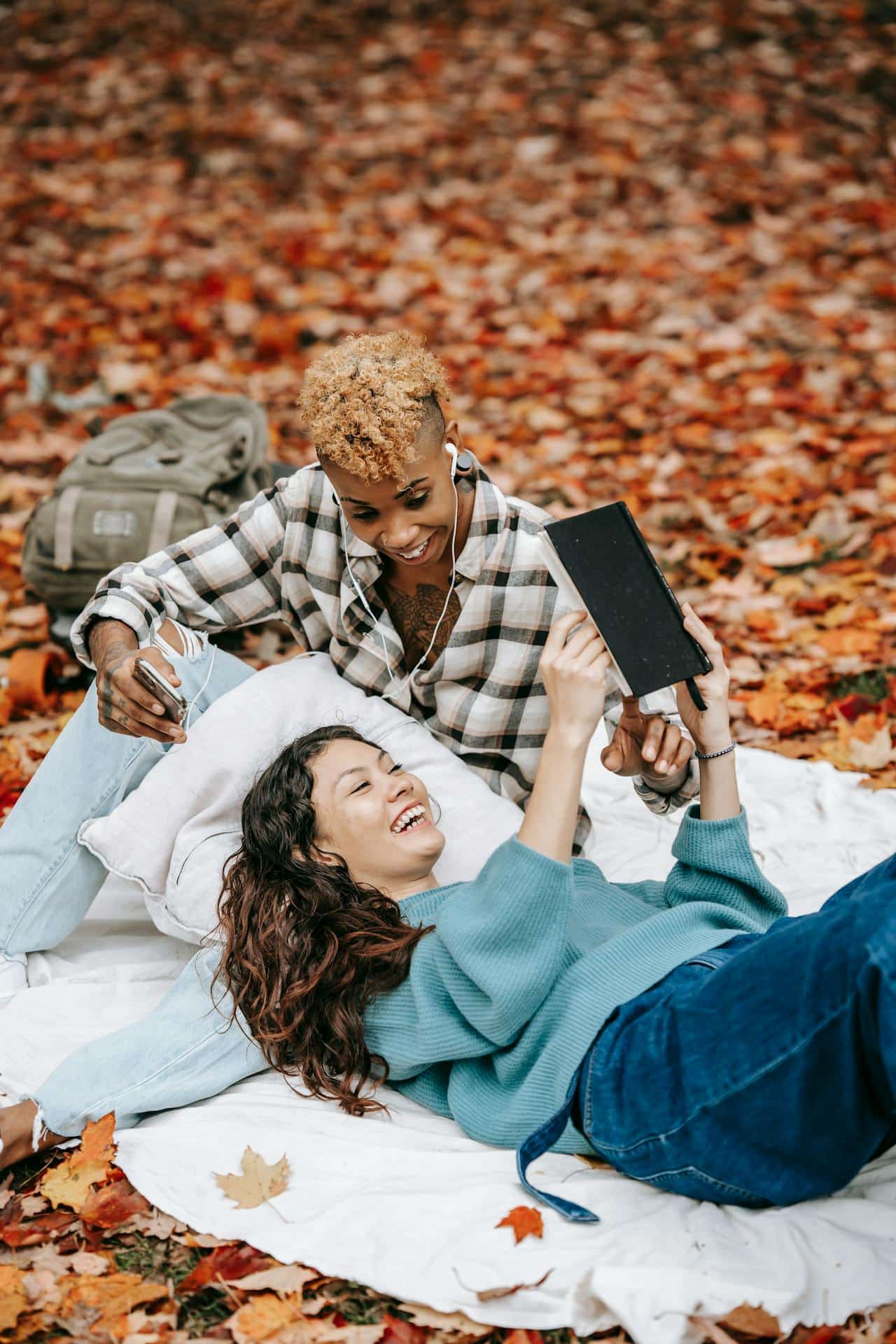 A bisexual couple, a white woman a Black woman, relaxing together in an outdoor Fall scene. 