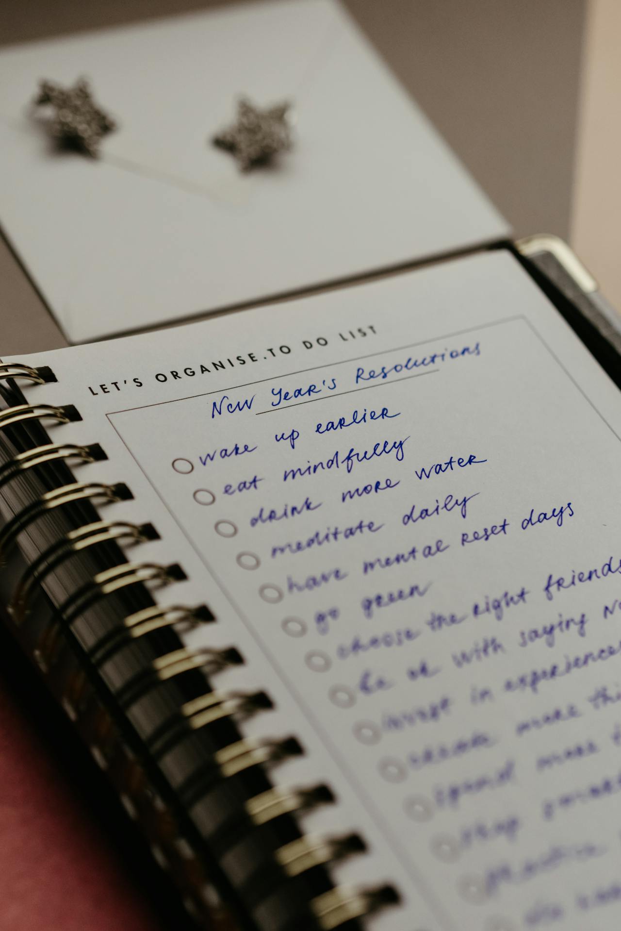 Close-up of a spiral notebook with a handwritten 'New Year's Resolutions' list, featuring goals such as 'wake up earlier' and 'drink more water.