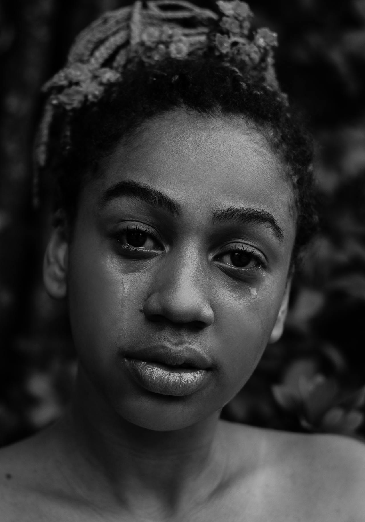 Black and white photo of a black woman with tears on their face, looking directly at the camera.